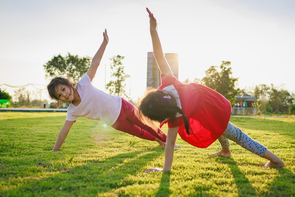 Children meditation with yoga pose on green grass field.